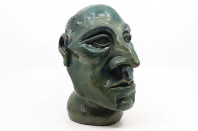 une sculpture verte représentant une tête d'homme sur une surface blanche
