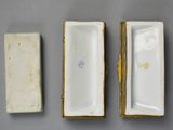 three small white porcelain boxes with gold trims on a gray surface