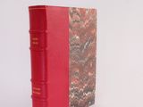 an old red book sitting on top of a white surface