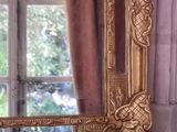 a gold mirror sitting on a window sill with a chandelier in the background