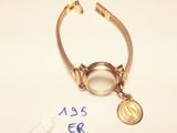 gold plated bracelet with a coin and a tag on a white surface