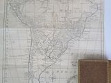 an old map of south america with a brown book on a table