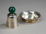 un plateau en argent surmonté d'une perle verte, à côté d'un bol en argent