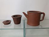 a brown teapot and a cup on a glass shelf