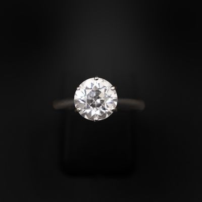 une bague en diamant posée sur une surface noire, avec un fond noir