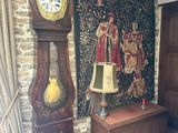 a grandfather clock in the corner of a room with a tapestry on the wall