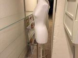 un mannequin blanc dans un coin d'une pièce, avec un rouleau de papier toilette par terre