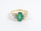un gros plan d'une bague en or sertie d'une pierre verte et de deux diamants blancs