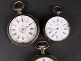 three antique pocket watches sitting on top of a black surface