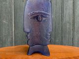 une statue bleue posée sur une table en bois, avec une clôture verte en arrière-plan