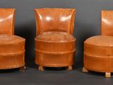 trois fauteuils en cuir marron placés les uns à côté des autres sur une surface noire