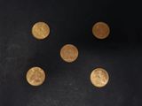 six pièces d'or sont disposées en cercle sur une surface noire