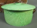a green pot with a lid sitting next to a brown plate
