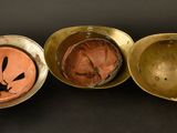 three antique brass bowls with faces on them on a black surface