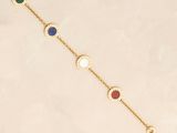 a gold bracelet with multi colored stones on a white background