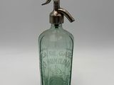 an old green glass bottle with a metal spout on a white surface
