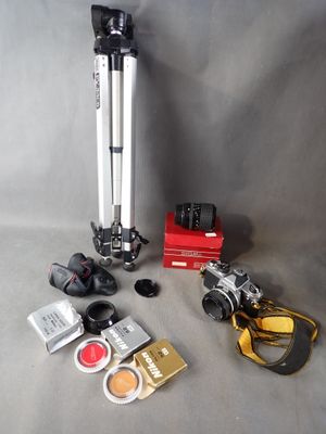 a camera, a tripod, a camera lens, a camera case, and other items laid out on a table