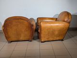 pair of brown leather club chairs in a room with tile flooring