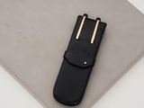 black leather pen case with two gold pins on top of a white surface