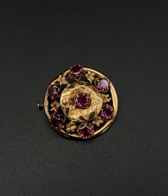 un gros plan d'une broche en or et rubis posée sur une surface noire
