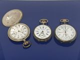 trois types différents de montres de poche exposées sur un fond bleu