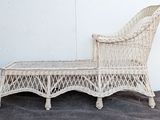 a white wicker chaise sitting against a white wall