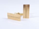 two gold cufflinks on a white surface with a white background