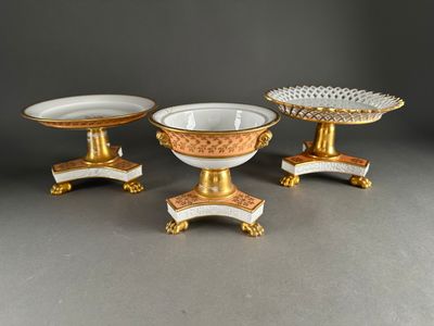 three pieces of gold and white porcelain on pedestals on a gray surface