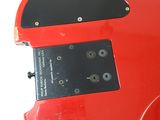 the back of a red electric guitar sitting on top of a white surface