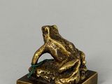 bronze figurine of a frog sitting on a rock with a leaf in its mouth