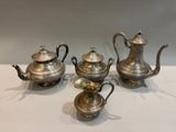 four pieces of silver tea set on a white table