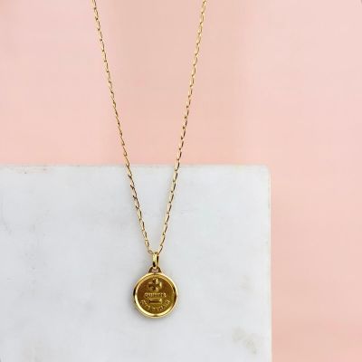 un collier composé d'une médaille en or suspendue à une chaîne en or, sur fond rose