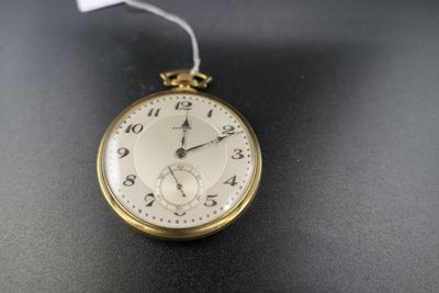 une montre de poche en or posée sur une surface noire, avec une étiquette blanche