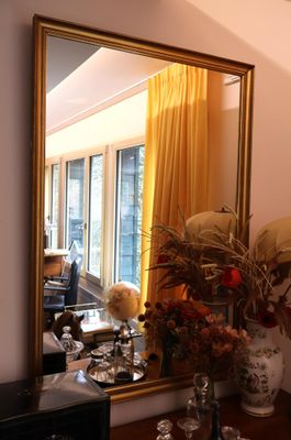 un miroir posé sur une table, devant lequel se trouve un vase de fleurs
