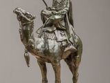 bronze statue of a man riding a camel with a spear in his hand