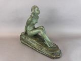 bronze statue of a woman sitting on a rock on a white background