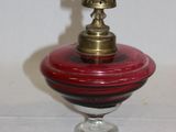 un petit bol en verre rouge avec un couvercle doré, posé sur une table