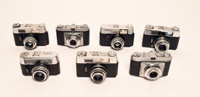 six old cameras are lined up in a row on a white surface