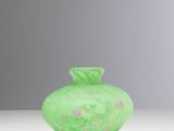 green glass vase with pink flowers on it sitting on a white surface