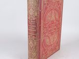 an old book with a red cover sitting on a white surface
