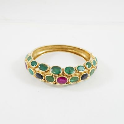 un gros plan d'une bague en or sertie de pierres vertes, roses et bleues