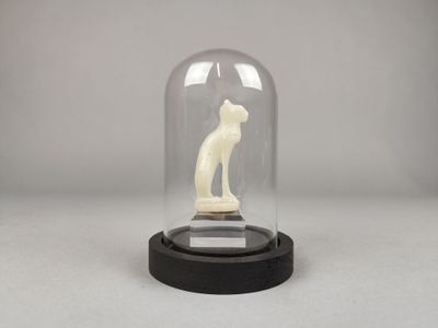 une photo représentant une statue de chat placée sous un dôme en verre, posée sur une table