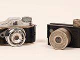 two old cameras sitting next to each other on a white surface