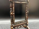 un miroir ancien en bois posé sur un pied, sur une surface grise