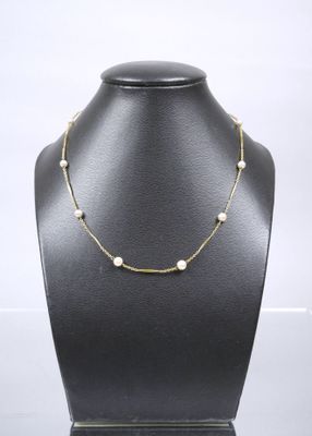 a gold necklace with pearls on a black mannequin
