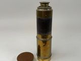 a small brass and black cylinder with a coin on a white surface