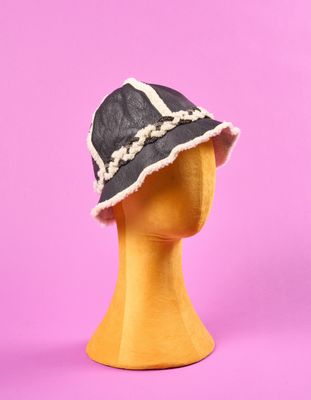un chapeau noir et blanc posé sur une tête de mannequin, sur fond rose