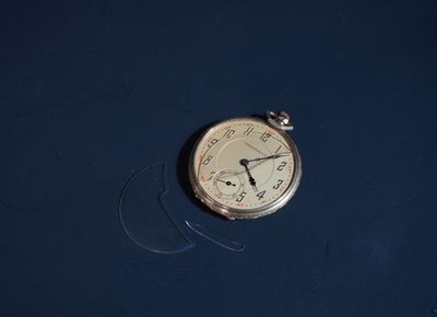 une montre de poche en argent posée sur une surface bleue