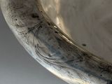 an old silver bowl sitting on top of a table next to a white wall
