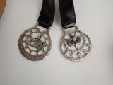 two silver medallions on a black leather strap